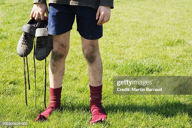 boy (8-10) standing in field, holding football boots, low section - muddy football pitch stock pictures, royalty-free photos & images