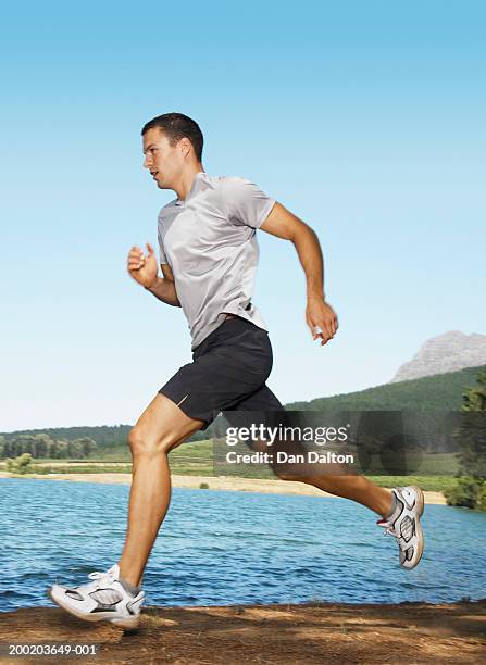 young man running by lake, side view - pantalón corto fotografías e imágenes de stock