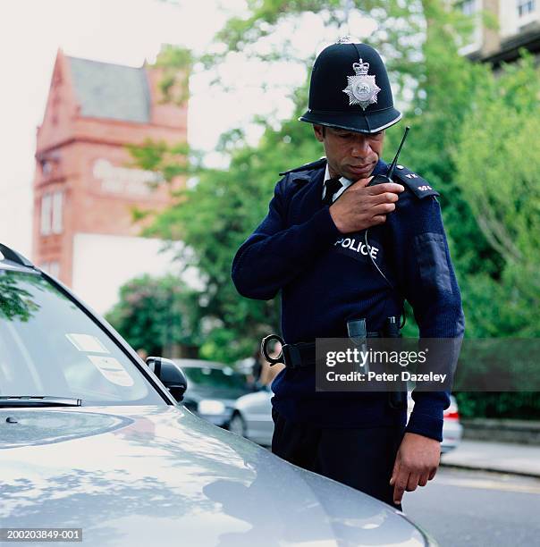 policeman standing by car using radio - cop car photos et images de collection