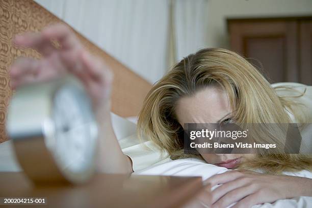 young woman on bed, reaching for clock - alarm clock on nightstand stock pictures, royalty-free photos & images