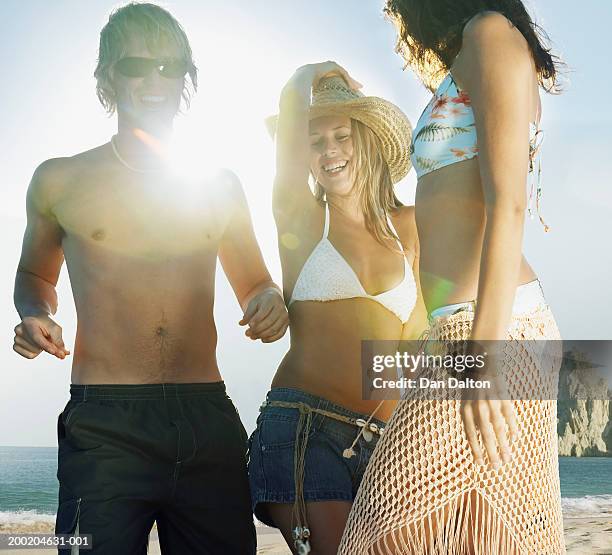three young friends dancing on beach, smiling (sun flare) - arm sun beach stock-fotos und bilder