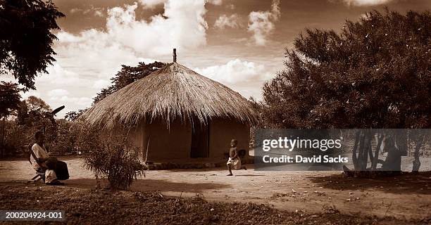 africa, uganda, woman watching girl (2-4) run beside hut (toned b&w) - thatched roof huts stock pictures, royalty-free photos & images