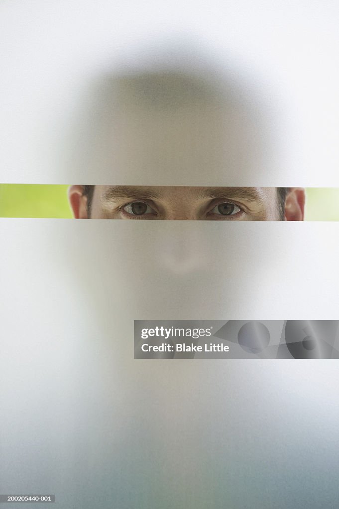 Man looking through frosted glass window, portrait (upper section)