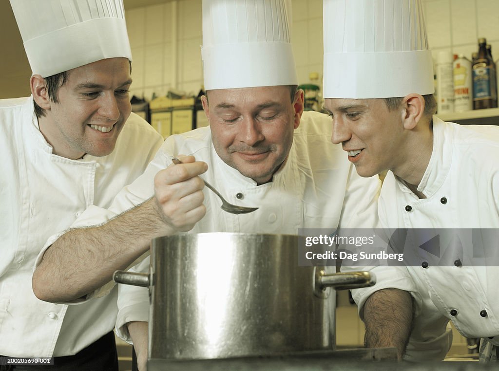 Three chefs looking over saucepan, close-up