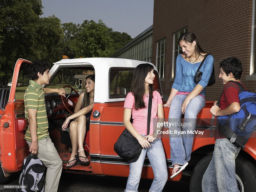 Five teenagers (14-16) talking beside pick-up truck, smiling