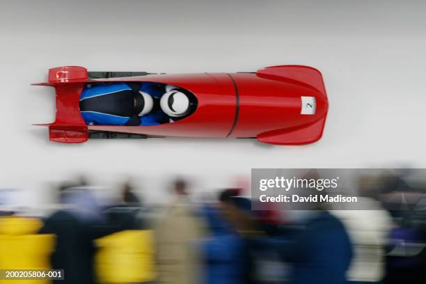 two-man bobsled racing down track, blurred crowd - bobrennschlitten stock-fotos und bilder