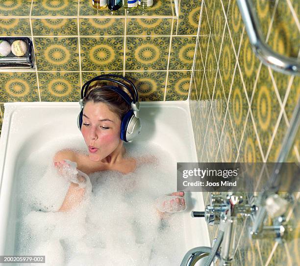 young woman wearing headphones in bath blowing foam from hand - bathtime foto e immagini stock