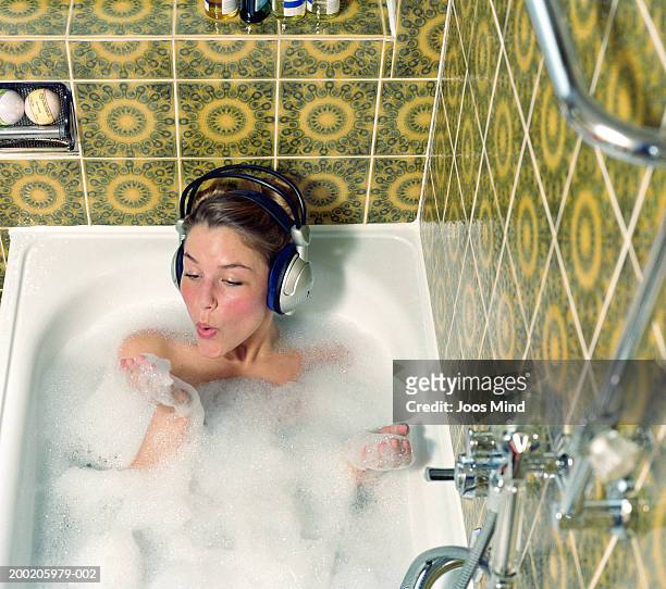 young woman wearing headphones in bath blowing foam from hand - bathtub stock pictures, royalty-free photos & images