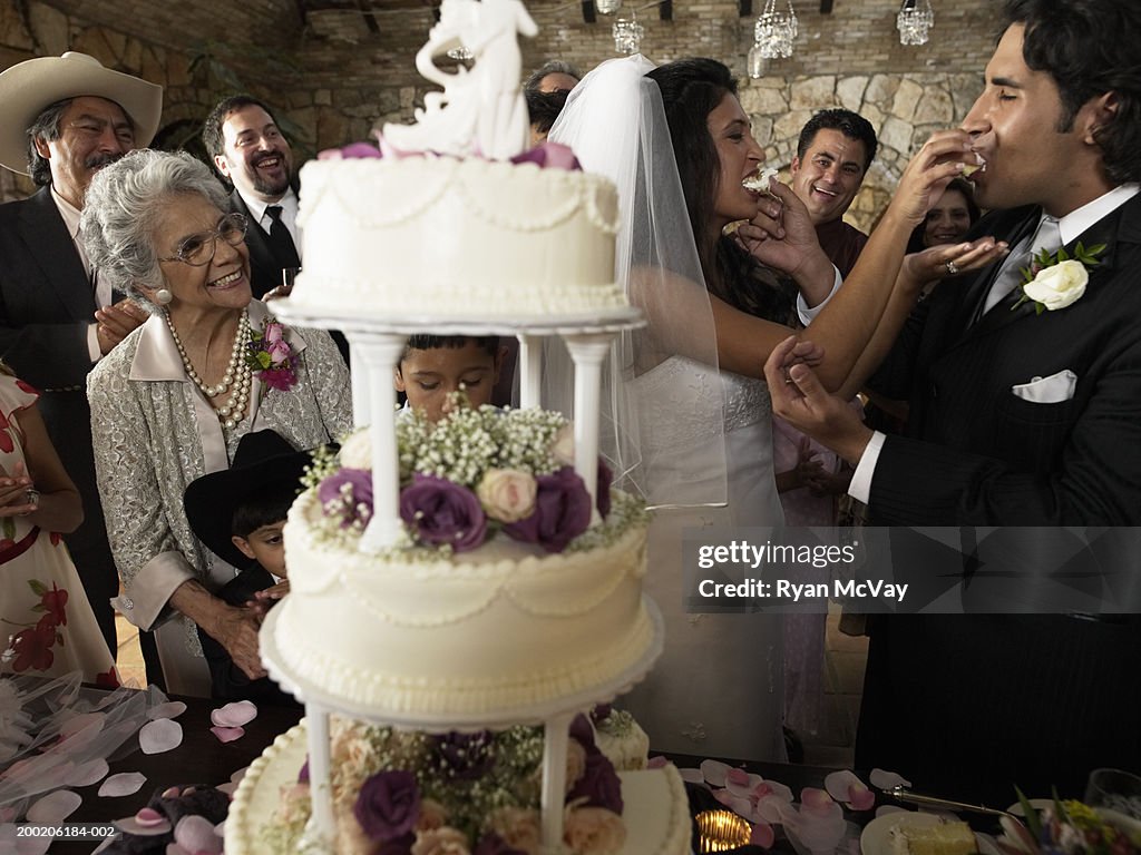 People watching bride and groom feed each other cake at reception