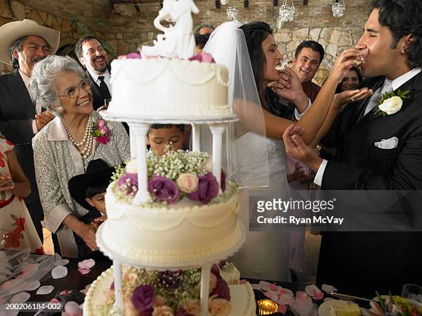 people watching bride and groom feed each other cake at reception - wedding cakes stock pictures, royalty-free photos & images