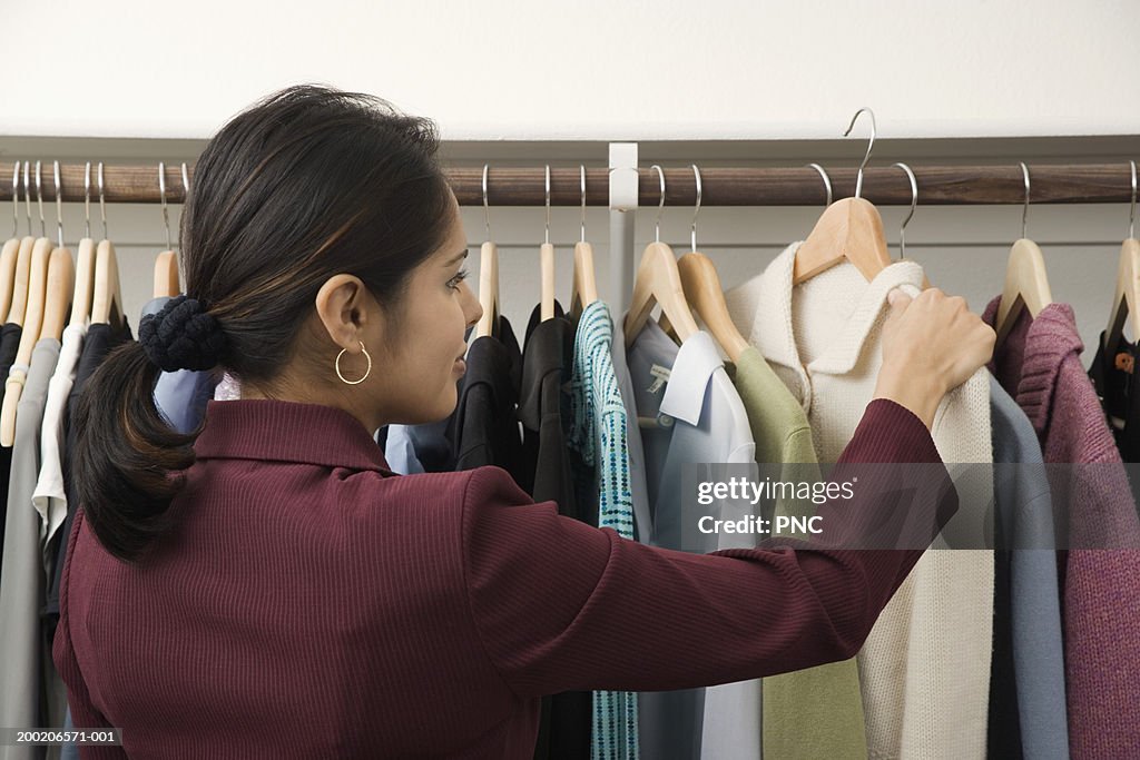 Young woman looking at sweater on clothes rack, rear view