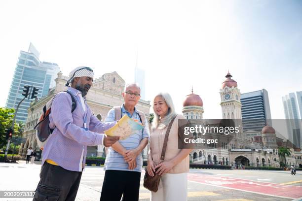 senior sikh tour guide explaining the history of the heritage sultan abdul samad buildings to two senior asian traveler at the merdeka square, kuala lumpur - abdul stock pictures, royalty-free photos & images