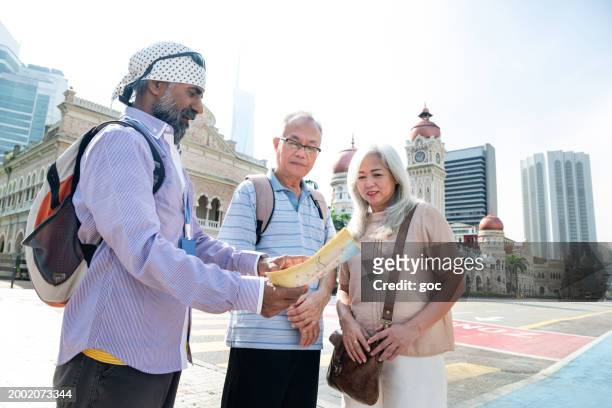 a mature sikh tour guide explaining about the heritage architecture and history of the sultan abdul samad buildings to two senior asian tourist - abdul stock pictures, royalty-free photos & images