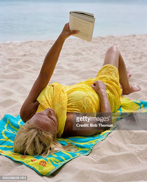 senior woman relaxing on beach, reading book - sarong stock pictures, royalty-free photos & images
