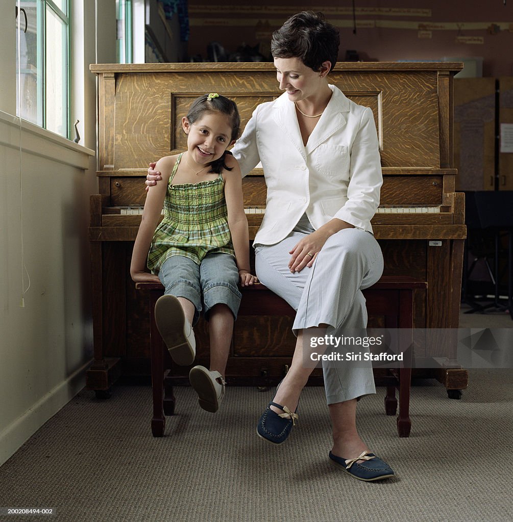 Piano teacher sitting in front of piano with student (4-6), portrait