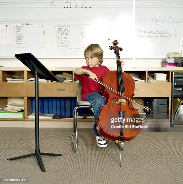 boy (5-7) playing cello in classroom - wonderkind stock-fotos und bilder