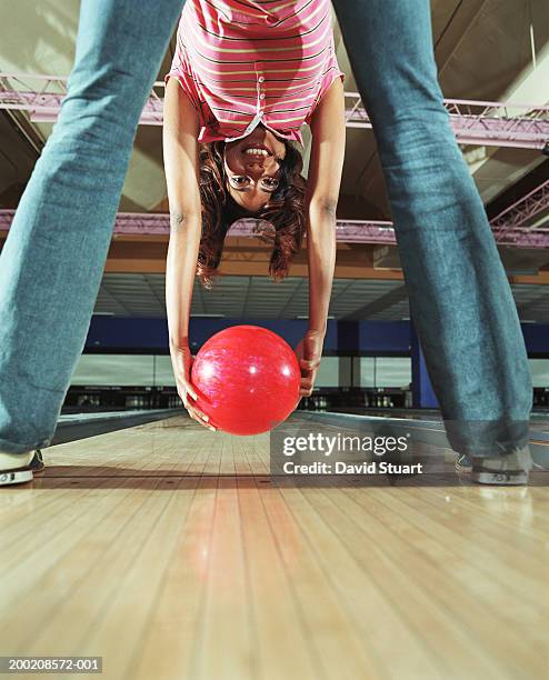 young woman holding bowling ball, framed by legs, smiling, portrait - bowling stock-fotos und bilder
