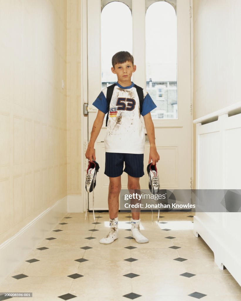 Boy (8-10) standing in hallway, holding football boots, portrait