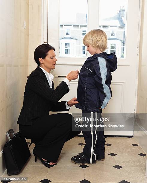 woman in suit zipping up son's (5-7) jacket at front door, side view - businesswoman in suit jackets stock-fotos und bilder