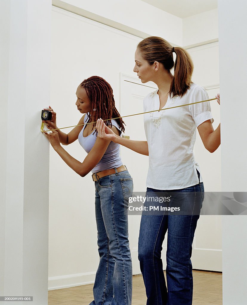 Two young women measuring doorway in apartment