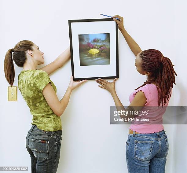 two women hanging picture on wall - hanging stock-fotos und bilder