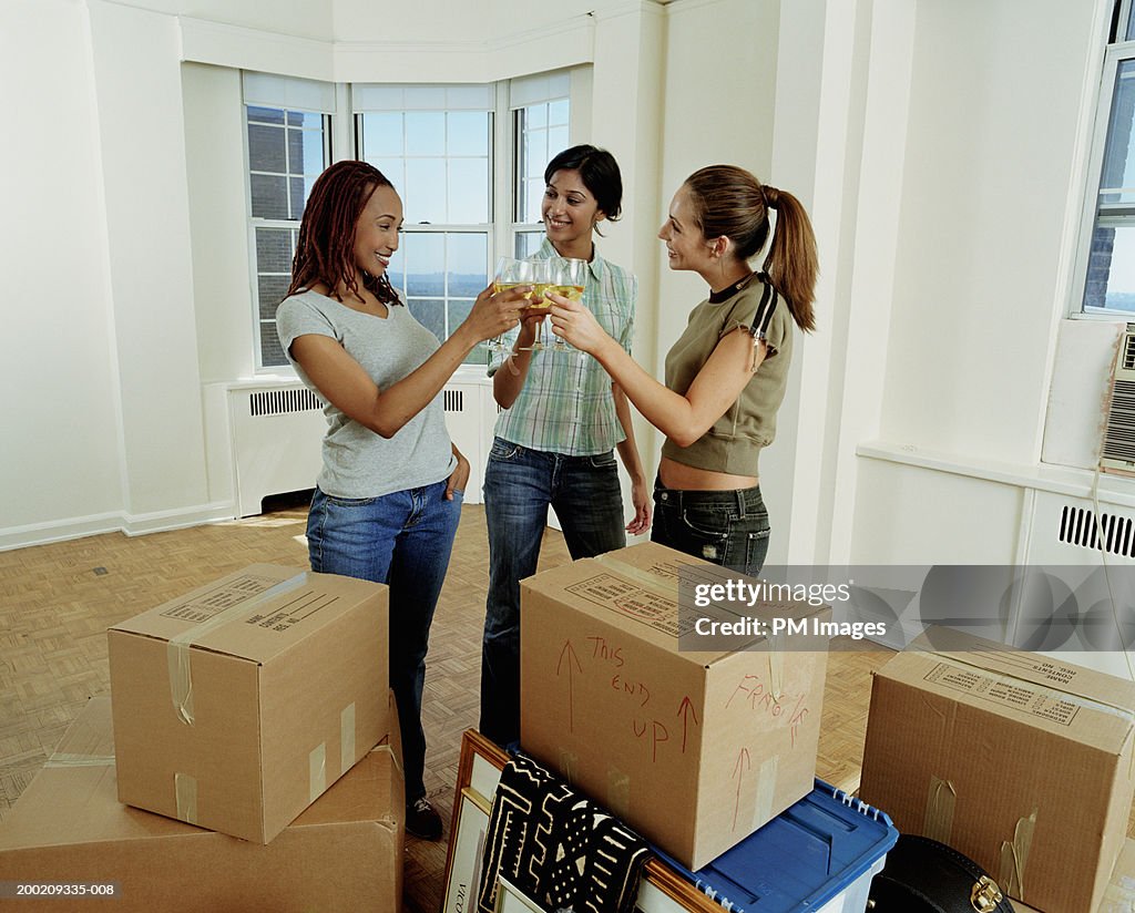 Three young women toasting drinks in apartment