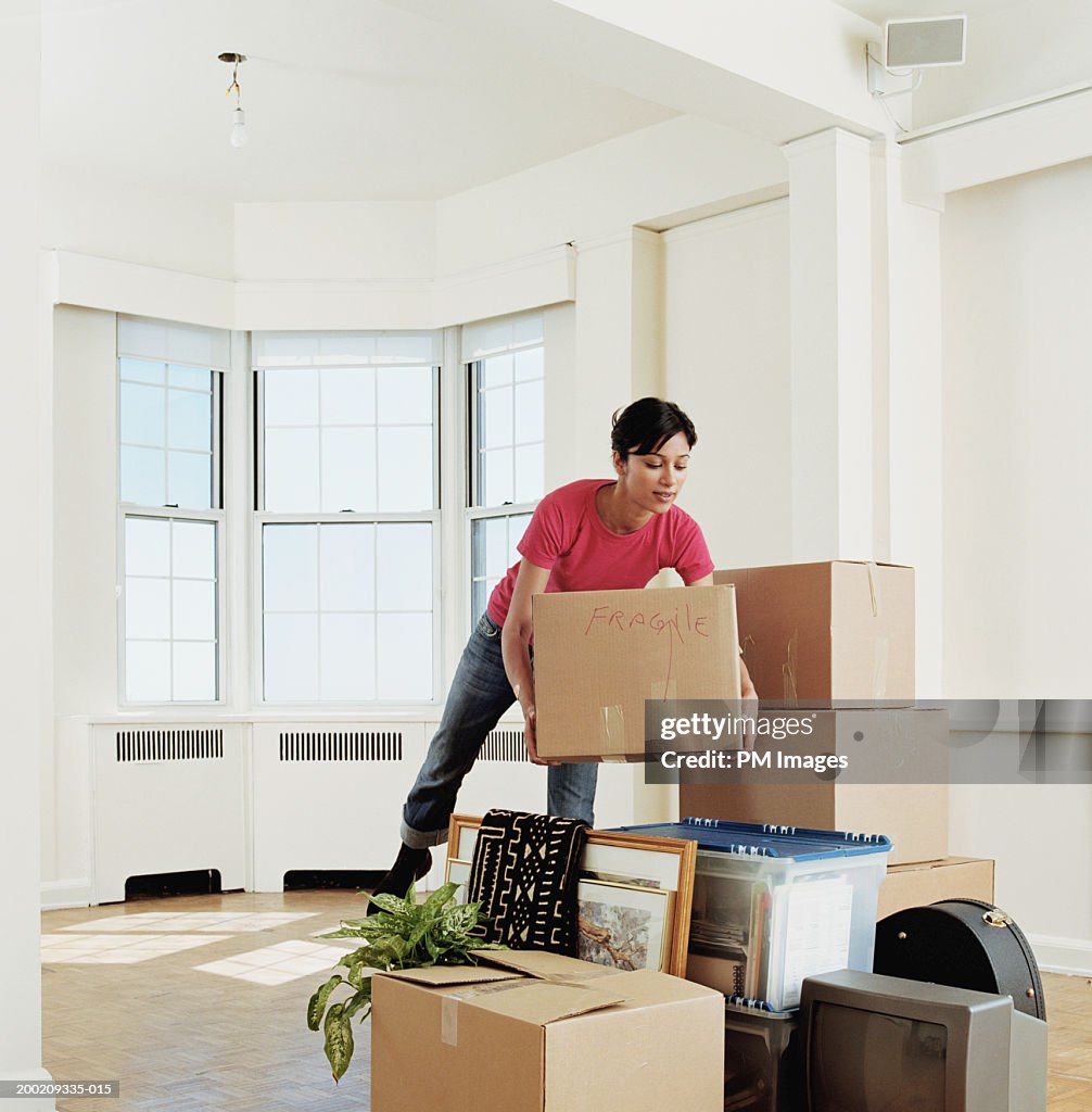 Young woman placing box on stack of belongings in apartment