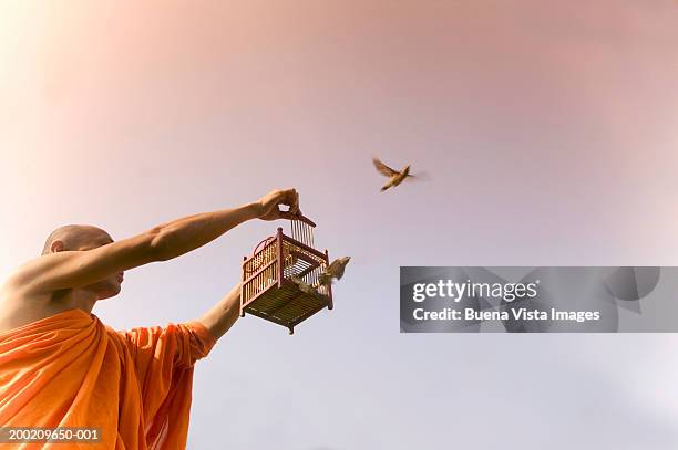 buddhist monk releasing birds from small cage, low angle view - releasing birds stock pictures, royalty-free photos & images