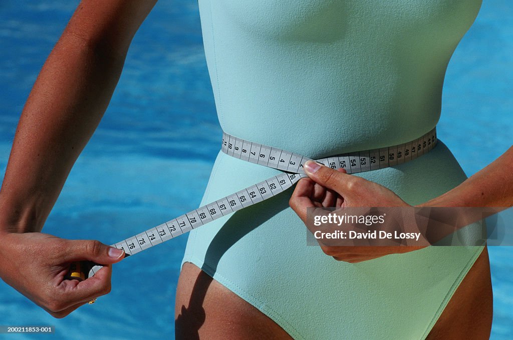 Woman with measuring tape around waist, mid section