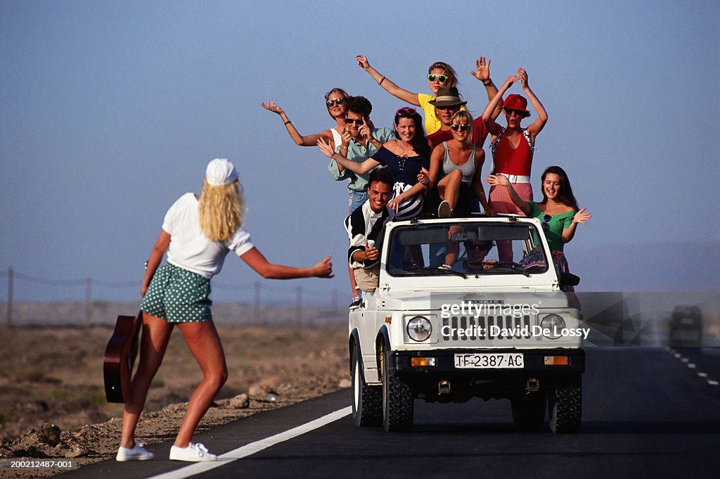 Woman with guitar asking lift from group of people in car