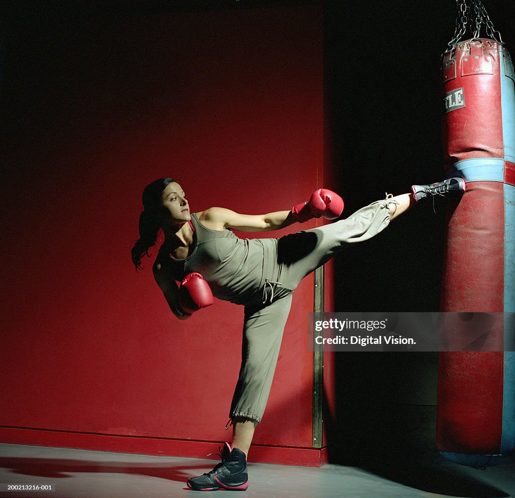 Young female boxer kicking punch bag