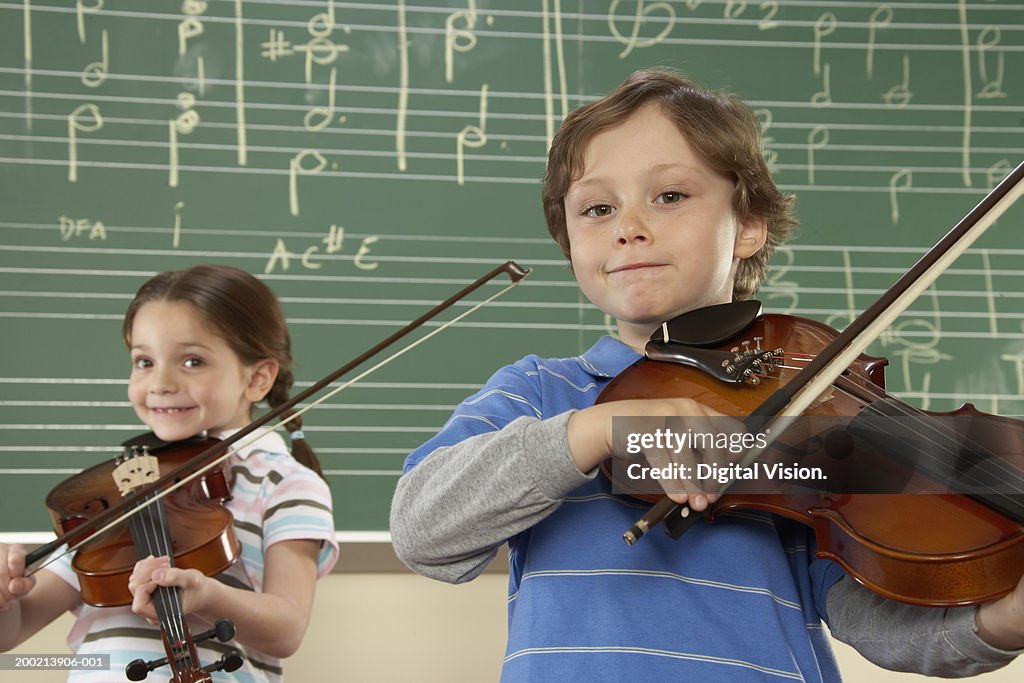 Girl and boy (5-10) playing violins in music class, smiling