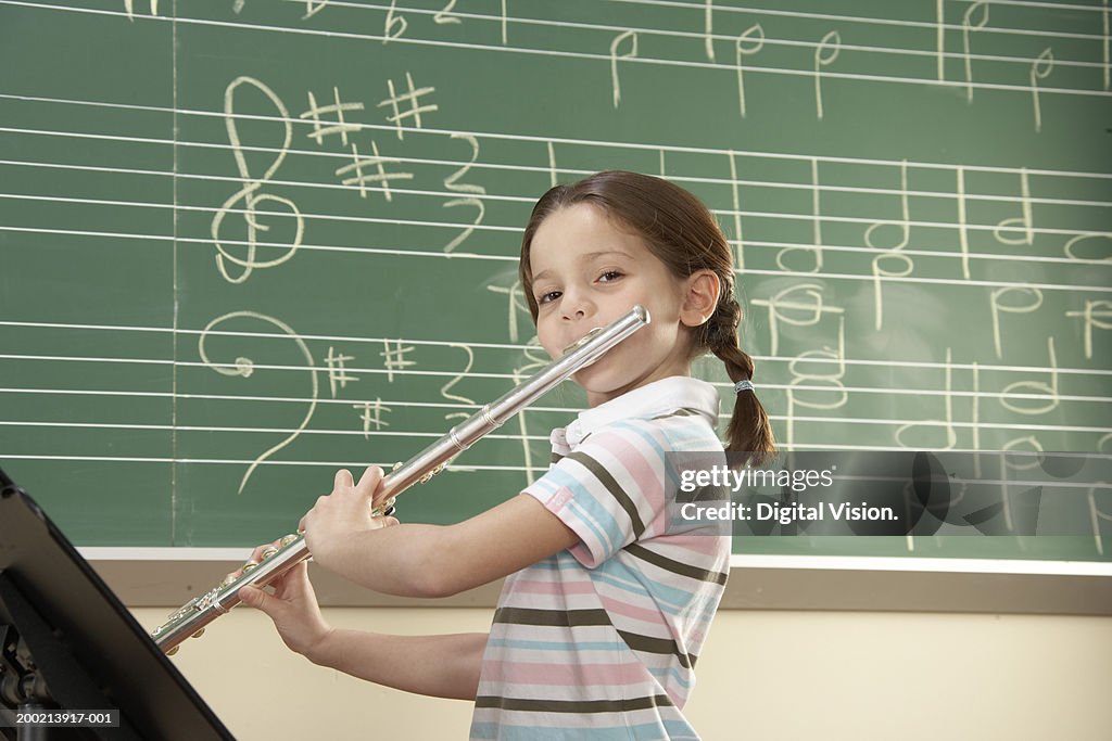 Schoolgirl (5-10) playing flute, smiling, portrait