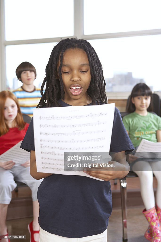 Schoolgirl (6-12) singing from music sheet in classroom