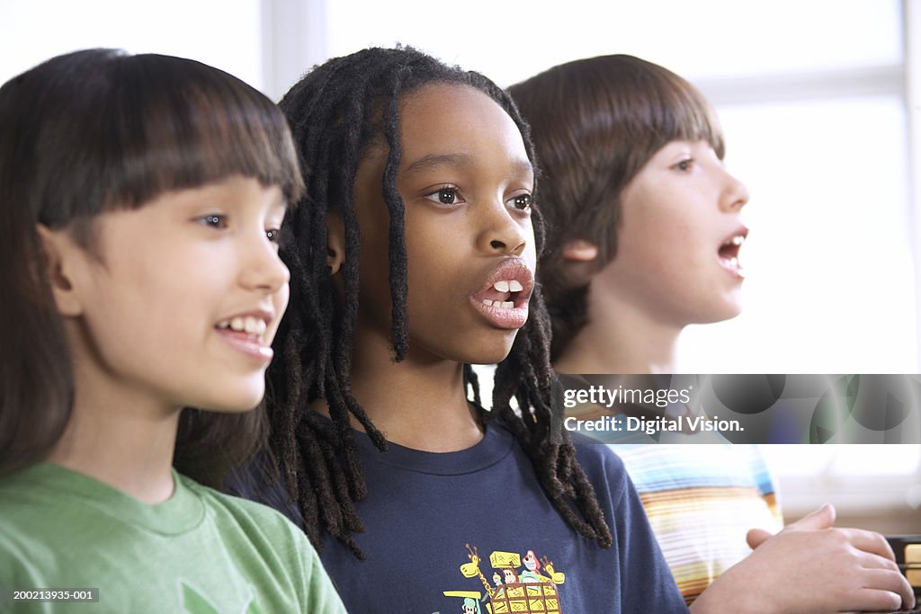 Two schoolgirls and schoolboy (6-12) singing in row, close-up