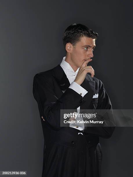 young man wearing tuxedo, holding finger to mouth, looking away - tuxedo stock pictures, royalty-free photos & images