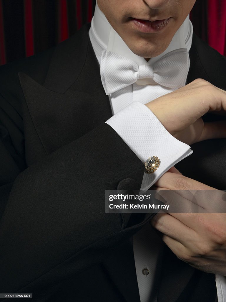 Man wearing tuxedo, adjusting cufflink, mid section, close-up