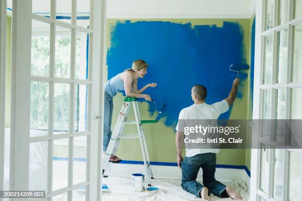 young couple conversing while painting wall - blue room stock pictures, royalty-free photos & images