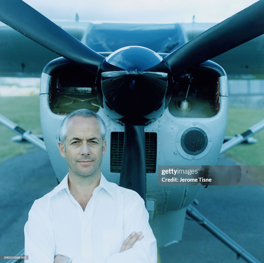 Mature man standing by plane, arms crossed, portrait