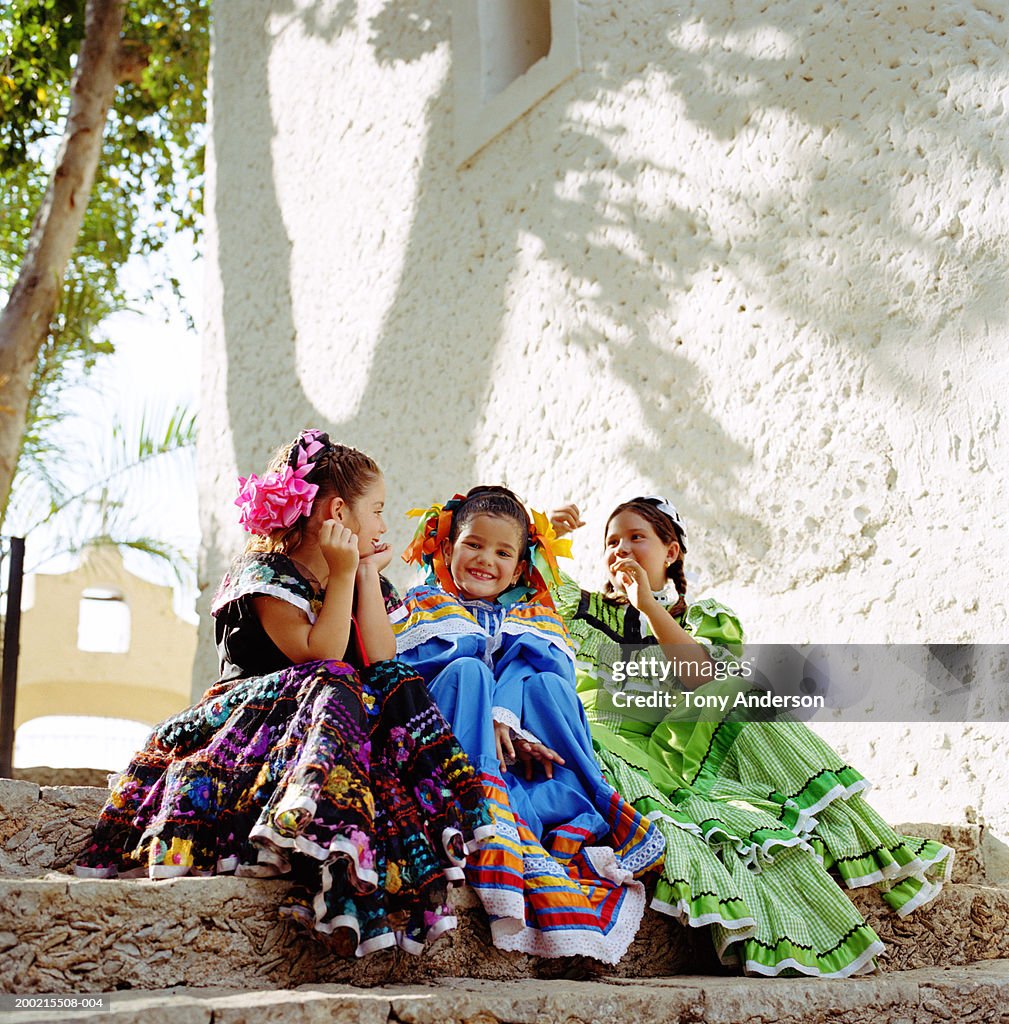 Three girls (5-9) wearing festival dresses, sitting on steps