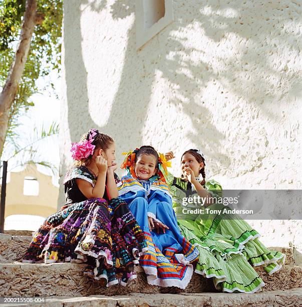 three girls (5-9) wearing festival dresses, sitting on steps - carnaval feestelijk evenement stockfoto's en -beelden