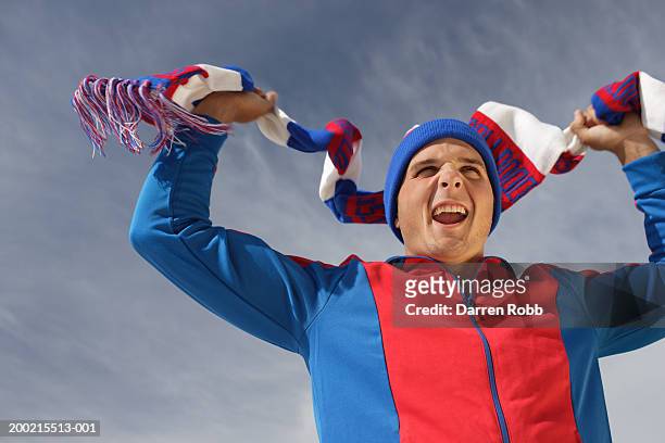 young man waving scarf above head, outdoors, low angle view - fan scarf bildbanksfoton och bilder