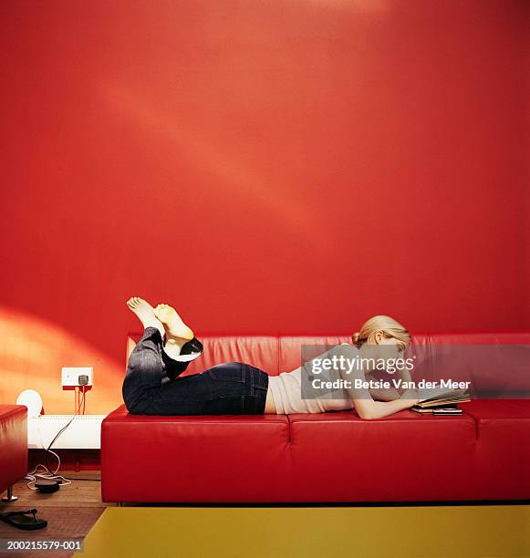 young woman lying on red sofa reading - donne bionde scalze foto e immagini stock