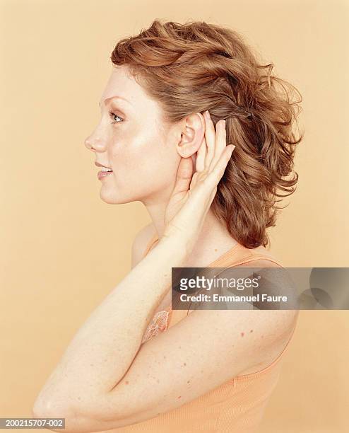 young woman cupping hand to ear, profile - hören stock-fotos und bilder