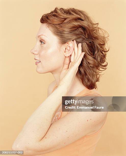 young woman cupping hand to ear, profile - oreja fotografías e imágenes de stock