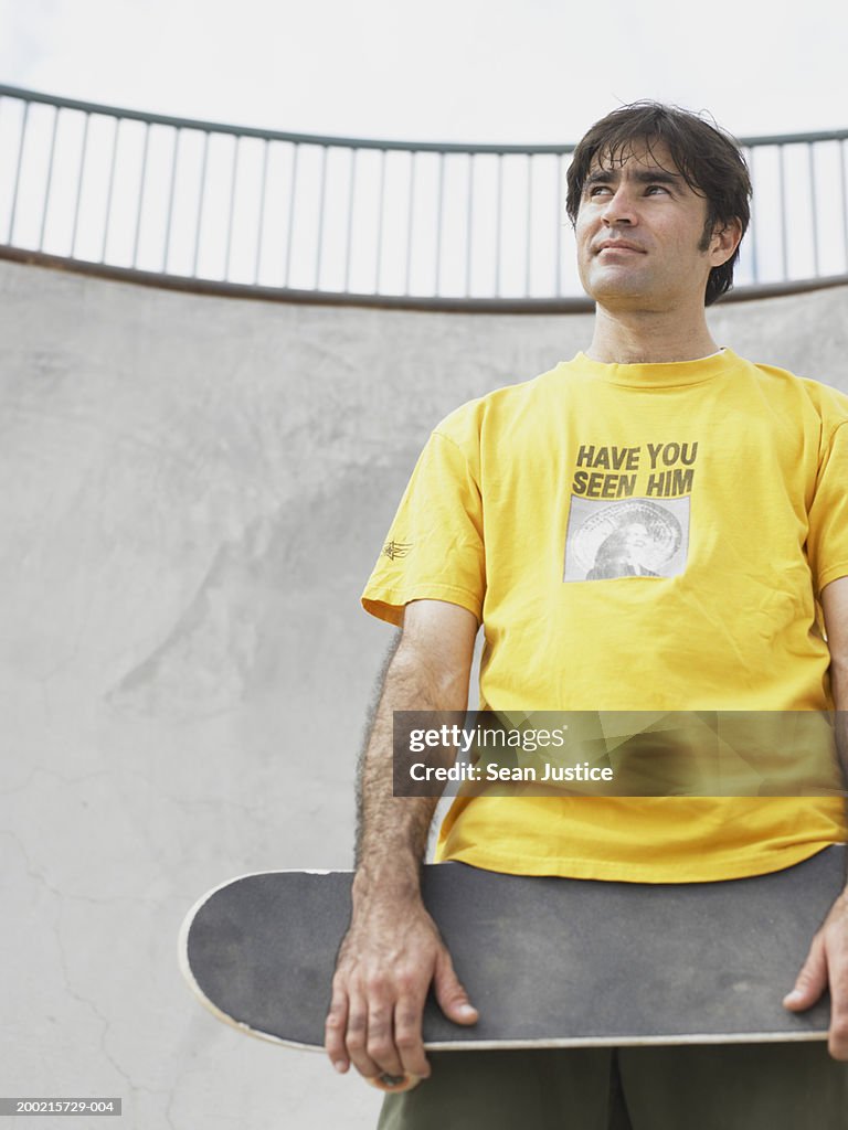 Man holding skateboard, looking away