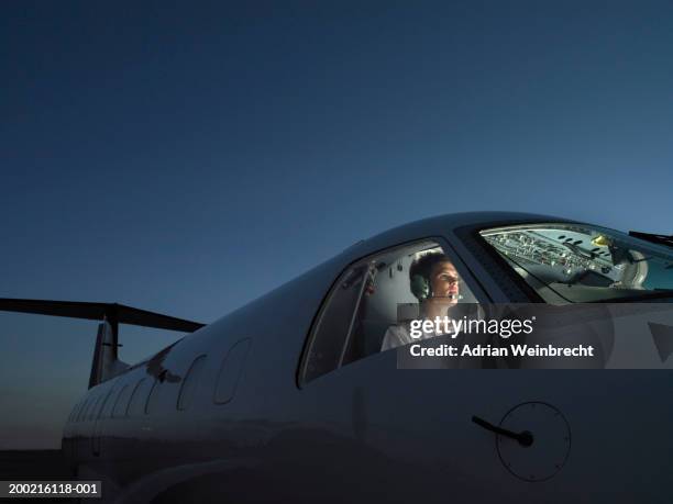 pilot in illuminated cockpit of plane wearing headphone, looking ahead - pilotar fotografías e imágenes de stock