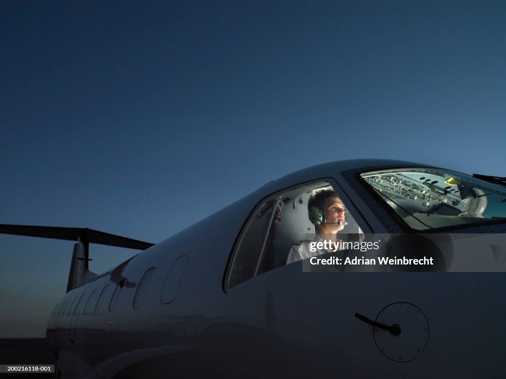Pilot in illuminated cockpit of plane wearing headphone, looking ahead