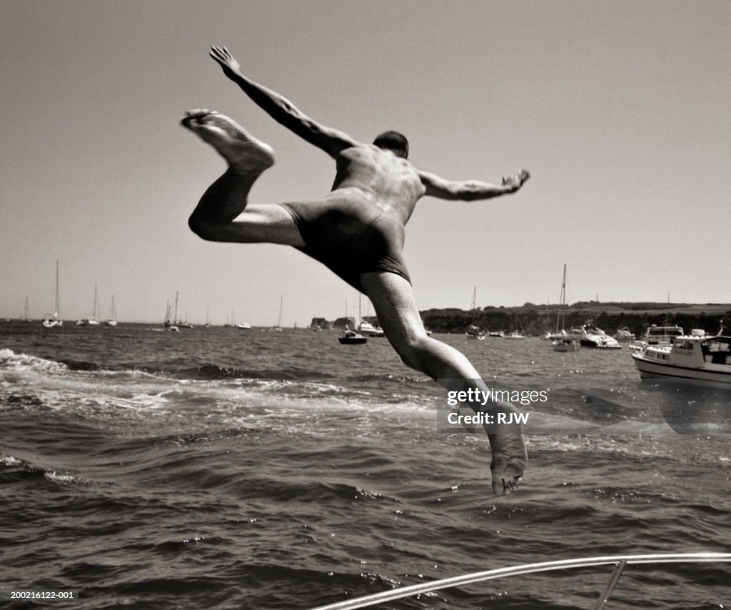 Man diving into sea from boat, rear view (B&W)