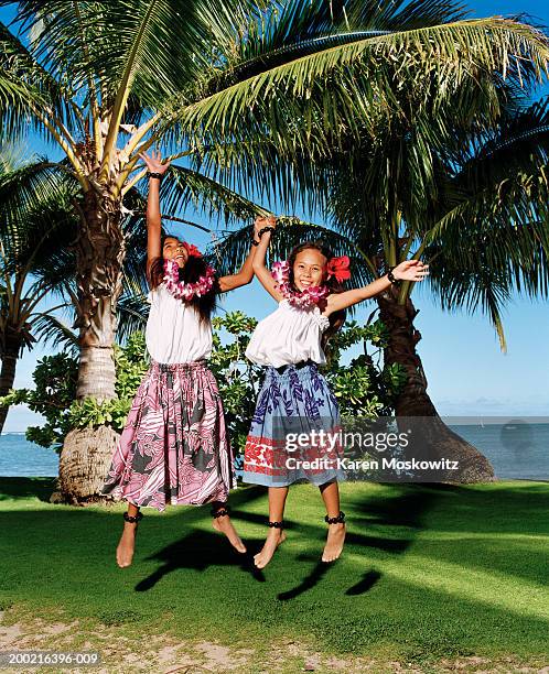 two girls (9-11) jumping in air, holding hands, arms raised, smiling - lei day hawaii stock-fotos und bilder